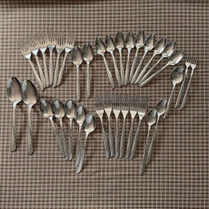 May include: A set of silver cutlery, including forks and spoons, arranged in a semi-circle on a brown and white checkered surface.