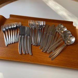 May include: A set of stainless steel silverware on a wooden tray. The set includes forks, knives, and spoons.