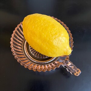 Puede incluir: Un lim&oacute;n amarillo en un plato de vidrio rosa con borde acanalado. El plato tiene un asa en el lateral.