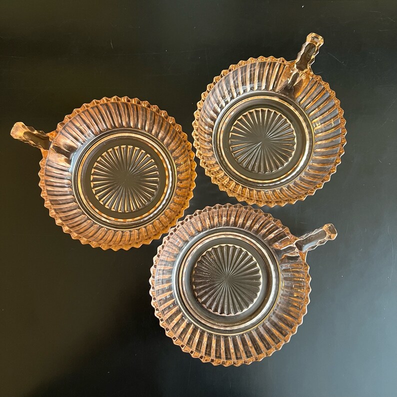 Puede incluir: Tres cuencos de vidrio vintage con asas. Los cuencos son de color rosa p&aacute;lido con un dise&ntilde;o acanalado. Los cuencos est&aacute;n vac&iacute;os y tienen un acabado brillante.