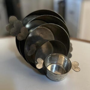 May include: A set of five silver nesting bowls with heart-shaped handles. The bowls are stacked on top of each other, with the smallest bowl on top.