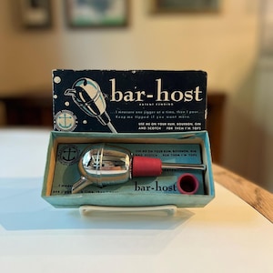 May include: Vintage "bar-host" liquor pourer in its original box. The chrome pourer has a red stopper and is packaged in a blue box with the product name and instructions. The box also features an anchor logo.