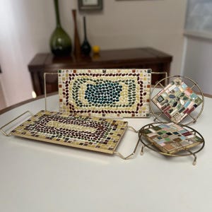 May include: Three mosaic tile trays with gold metal frames. The trays are decorated with colorful mosaic tiles in various patterns. The largest tray has a green and yellow pattern, the medium tray has a red and yellow pattern, and the smallest tray has a multi-colored pattern.