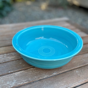 May include: A turquoise blue ceramic bowl with a ring design in the center. The bowl is sitting on a wooden surface.