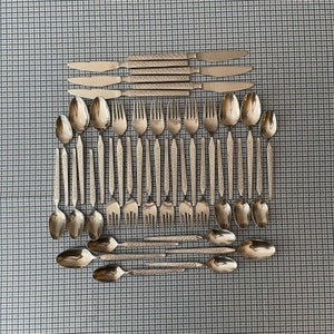 May include: A set of silver flatware, including forks, spoons, and knives, arranged in a grid pattern on a blue and white checkered tablecloth.