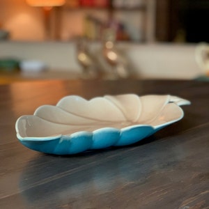 May include: A light blue and white ceramic serving dish shaped like a leaf. The dish has a scalloped edge and a smooth, glossy finish.