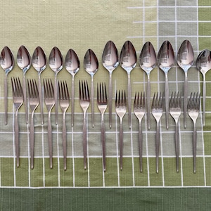 May include: A set of 18 silver-toned utensils, including spoons and forks, arranged in a row on a green and white checkered tablecloth.