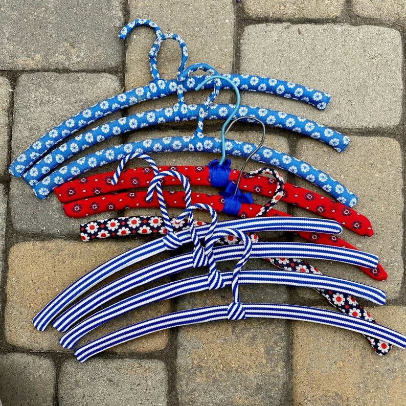 Puede incluir: Un conjunto de nueve perchas coloridas con un patr&oacute;n de rayas azules y blancas y patrones florales rojos, blancos y azules. Las perchas son de pl&aacute;stico y tienen un gancho de alambre.
