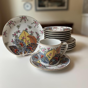 May include: A set of white porcelain teacups and saucers with a colorful floral pattern featuring leaves and flowers. The set includes a teacup and saucer with a matching design.