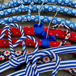 Puede incluir: Un conjunto de cuatro perchas coloridas con tela a rayas azul y blanca y tela roja con patrones florales blancos y azules. Las perchas est&aacute;n hechas de un material resistente y son perfectas para colgar ropa.