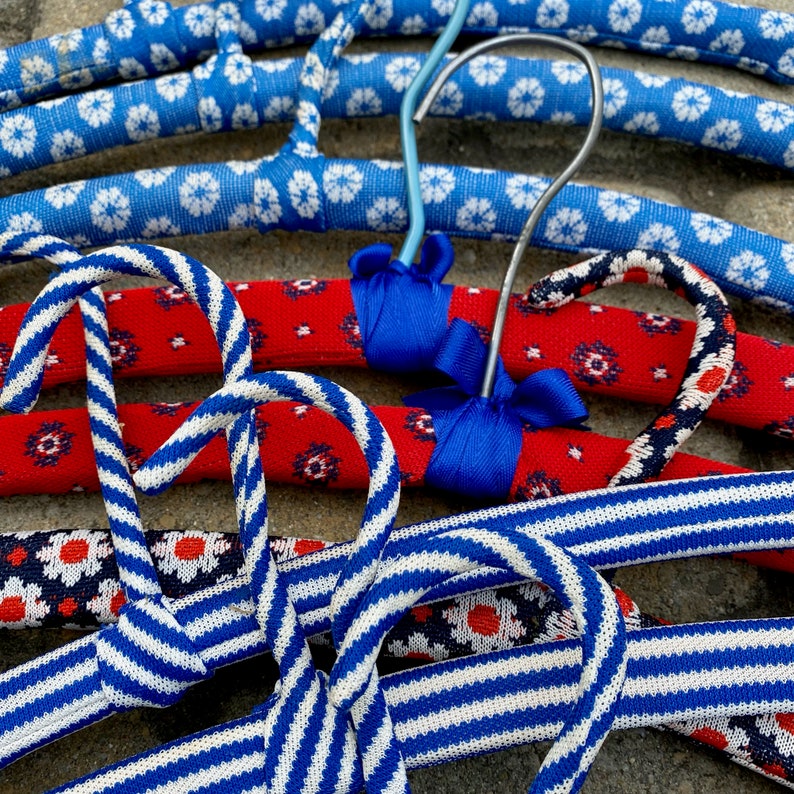 Puede incluir: Un conjunto de cuatro perchas coloridas con tela a rayas azul y blanca y tela roja con patrones florales blancos y azules. Las perchas est&aacute;n hechas de un material resistente y son perfectas para colgar ropa.
