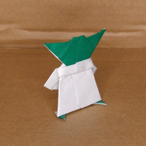 May include: Green and white origami figure of Yoda from Star Wars. The figure is standing with its arms outstretched.