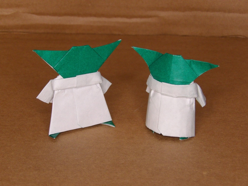 May include: Two origami Yoda figures, one facing forward and one facing backward. Both figures are made of green and white paper.