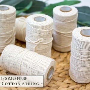 Puede incluir: Seis carretes de hilo de algodón blanco natural de 1 mm, dispuestos sobre una superficie de mimbre tejido.  LOOM & FIBRE - 1MM COTTON STRING - está impreso en una etiqueta blanca.