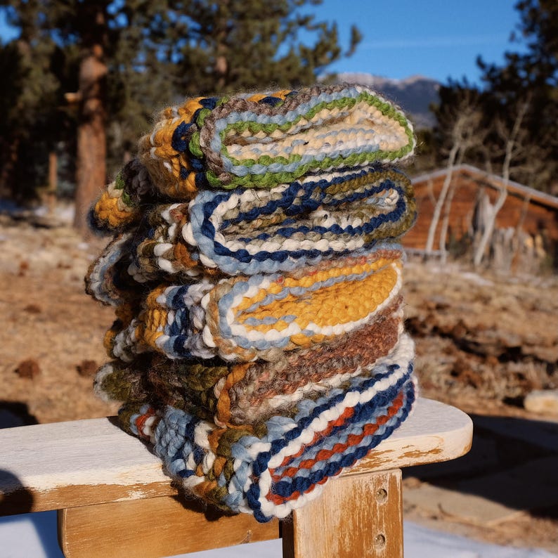 May include: A stack of colorful woven blankets with different patterns and textures. The blankets are folded and stacked on a wooden surface.