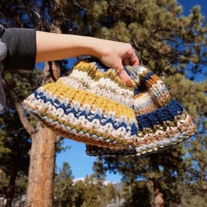 May include: Two knitted hats in a colorful striped pattern of blue, yellow, white, and green. The hats are held in a hand.