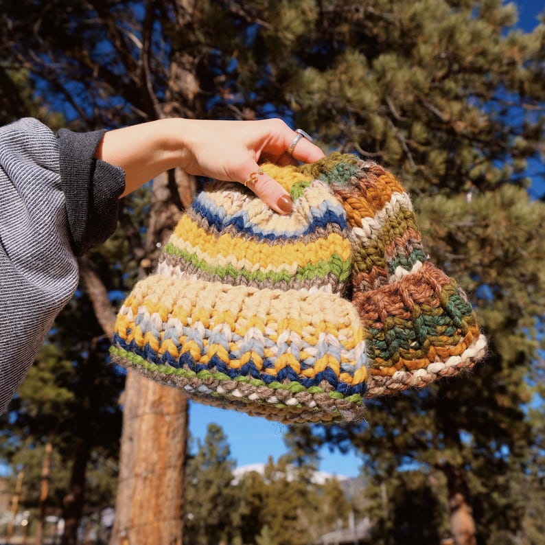 May include: Two knitted hats in a colorful striped pattern. One hat is brown, green, and yellow, and the other is beige, blue, and yellow.
