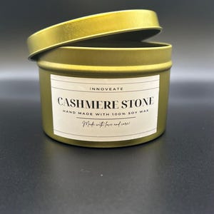 May include: A gold metal candle tin with a white label that reads "INNOVEATE CASHMERE STONE HAND MADE WITH 100% SOY WAX Made with love and care!"