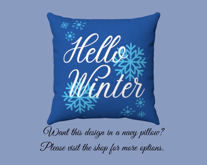 Pode incluir: Uma almofada quadrada azul marinho com as palavras "Hello Winter" em branco, acompanhada por desenhos de flocos de neve azul claro. Um item decorativo para a decora&ccedil;&atilde;o de inverno.
