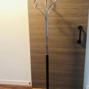 Peut inclure: Un porte-manteau en chrome avec une base noire et six crochets circulaires. Le porte-manteau est pos&eacute; sur un sol en bois.