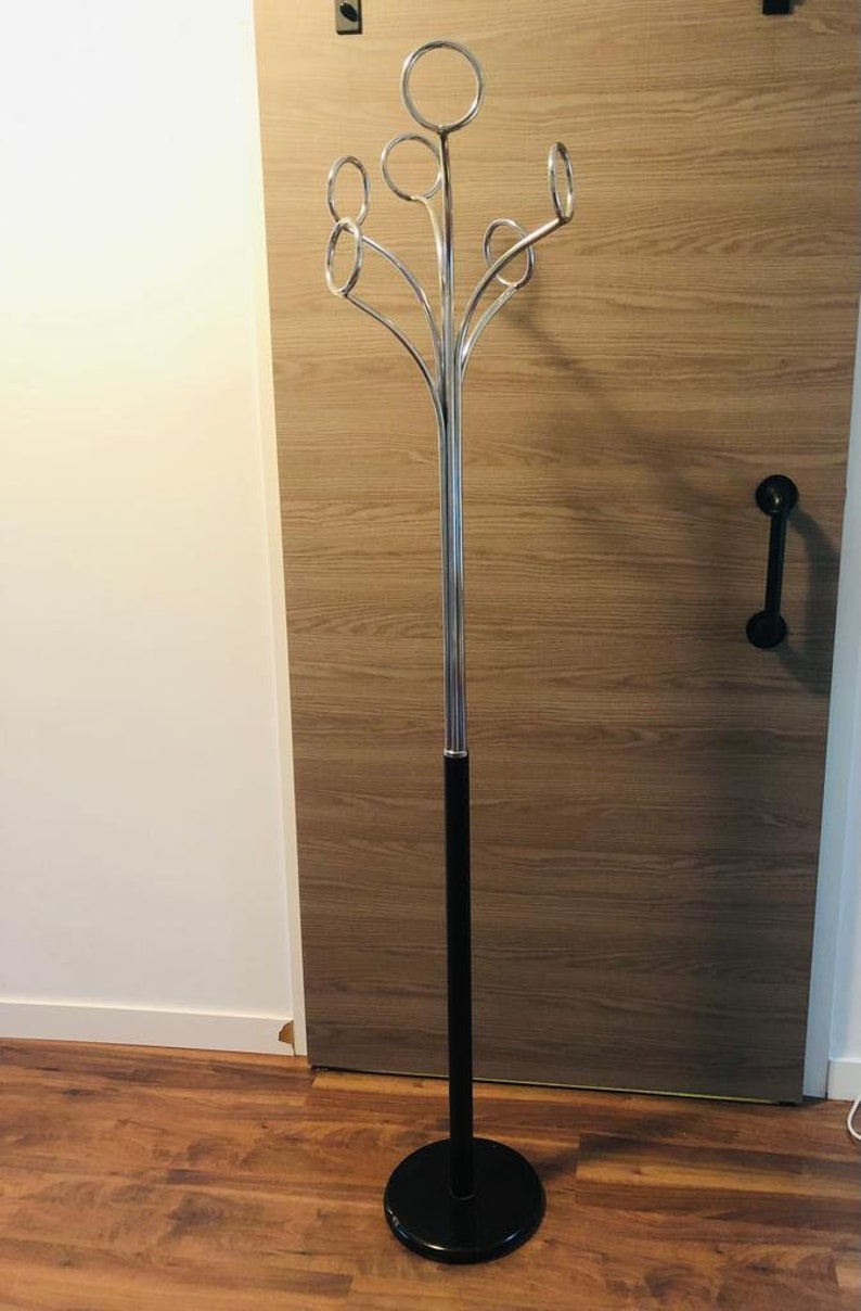 Peut inclure: Un porte-manteau en chrome avec une base noire et six crochets circulaires. Le porte-manteau est pos&eacute; sur un sol en bois.