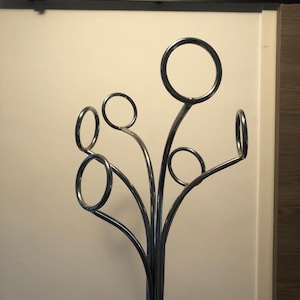 Peut inclure: Un porte-manteau en chrome avec un design en forme d'arbre. Le porte-manteau a six crochets en forme de cercles.