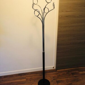 Peut inclure: Un porte-manteau noir et chrom&eacute; avec une base ronde et cinq crochets incurv&eacute;s. Le porte-manteau est pos&eacute; sur un sol en bois.