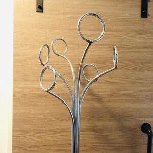 Peut inclure: Un porte-manteau en m&eacute;tal chrom&eacute; avec cinq crochets incurv&eacute;s. Le porte-manteau a une base haute et fine et un design moderne.
