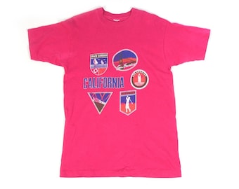 May include: A pink t-shirt with a graphic design featuring various California landmarks and the word "CALIFORNIA" in blue lettering.