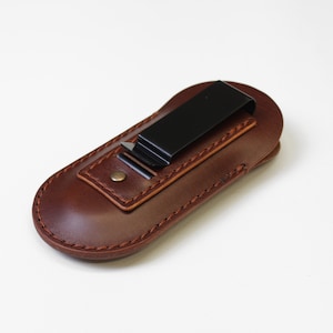 Peut inclure: Un étui en cuir marron avec un clip en métal noir. L'étui est conçu pour contenir un petit outil ou un couteau.