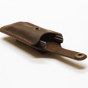 Könnte beinhalten: Ein braunes Lederetui mit Druckknopfverschluss und einem braunen Lederriemen. Das Etui ist geöffnet und ein silbernes Multitool befindet sich darin.