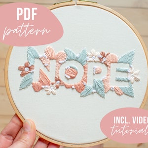 Könnte beinhalten: Ein Stickrahmen mit dem Wort "NOPE" in Weiß, umgeben von gestickten Blüten und Blättern in Pfirsich, Hellblau und Weiß. Der Text "PDF pattern" und "INCL. VIDEO tutorials" sind ebenfalls sichtbar.