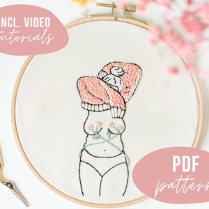 Könnte beinhalten: Stickbild in einem Stickrahmen mit einer Linienzeichnung einer Person, aus deren Brust Blumen wachsen, die einen rosa Pullover und Unterwäsche trägt. Der Rahmen befindet sich auf einem weißen Hintergrund mit einem rosa Oval mit dem Text "PDF pattern" und einem rosa Oval mit dem Text "INCL. VIDEO tutorials".