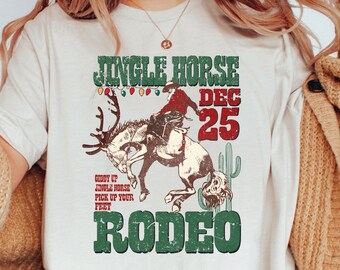 May include: White t-shirt with a vintage-style graphic of a reindeer being ridden by a cowboy. The graphic says "Jingle Horse Rodeo" and "Dec 25".