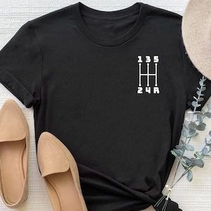 May include: Black t-shirt with a white graphic of a stick shift pattern with the numbers 1, 3, 5, 2, 4, and R.