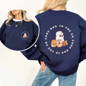 May include: A navy blue sweatshirt with a white circle graphic on the back. The graphic features a ghost wearing a nurse's hat and holding a bandage, surrounded by pumpkins. The text "BOO IN THE ER CODE" is written around the circle.