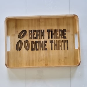 Op de afbeelding: Een houten dienblad met de tekst "BEAN THERE DONE THAT!" en twee koffieboonafbeeldingen die in het oppervlak zijn gebrand.