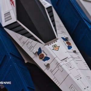 May include: A white and blue model spaceship with the words "Star Fox" and "SF" printed on the side. The spaceship has a black cockpit and a blue wing.