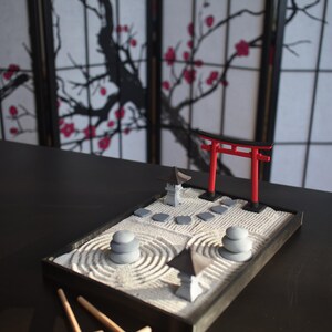 May include: A miniature zen garden with a red torii gate, gray stones, and a sand rake. The garden is set on a black tray and is surrounded by a black background.