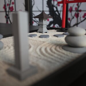 May include: A miniature zen garden with a gray pagoda, a red torii gate, and white stones on a white sand base.