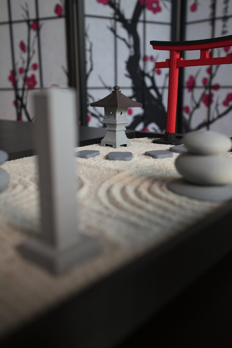 May include: A miniature zen garden with a gray pagoda, a red torii gate, and white stones on a white sand base.