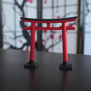 May include: A red and black miniature torii gate, a traditional Japanese gateway, on a black surface.