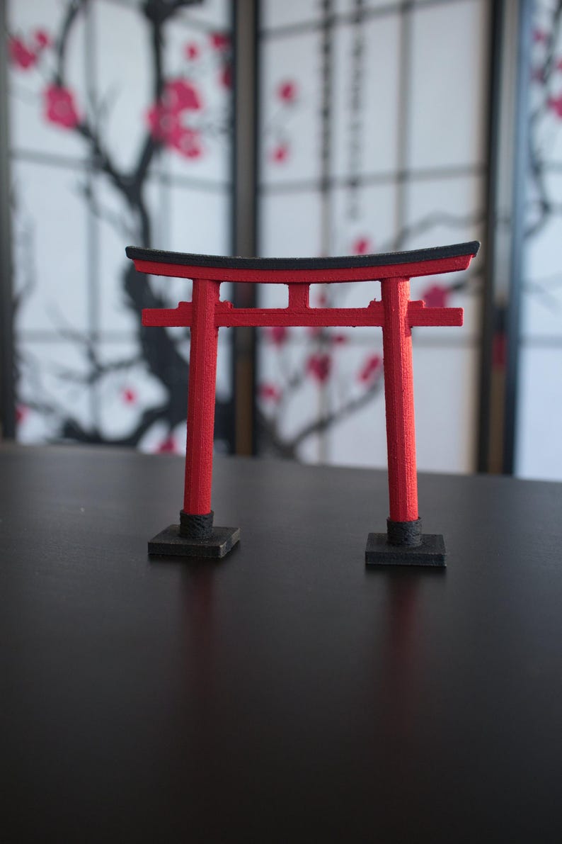 May include: A red and black miniature torii gate, a traditional Japanese gateway, on a black surface.