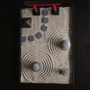 May include: A miniature zen garden with a red torii gate, gray rocks, and sand raked into patterns.