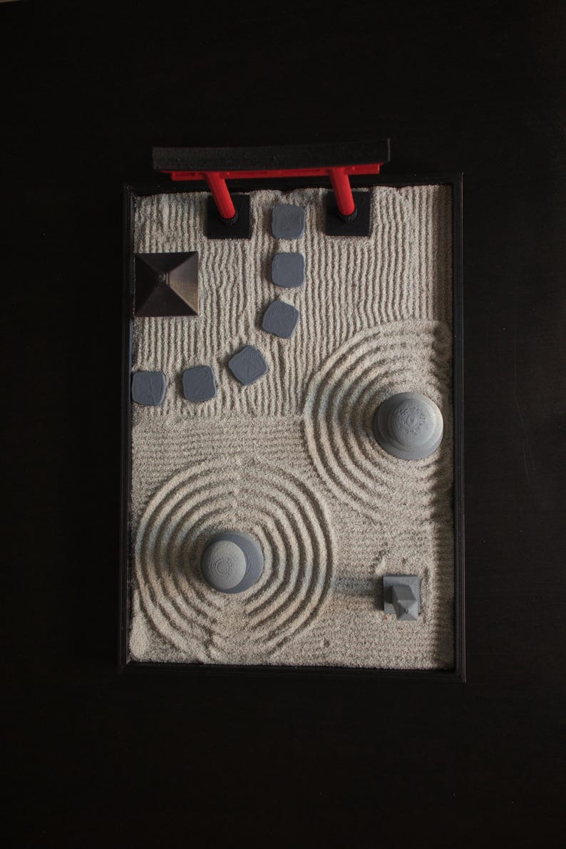 May include: A miniature zen garden with a red torii gate, gray rocks, and sand raked into patterns.