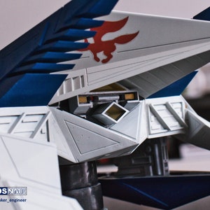 May include: A white and blue model airplane with a red and white fox logo on the wing. The model is detailed with a cockpit and a variety of panels and hatches. Designed by DSNNME.