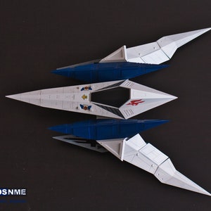 May include: A white and blue model spaceship with red and yellow accents. The spaceship has a pointed nose and two sets of wings. The wings are folded down and the spaceship is sitting on a dark surface.