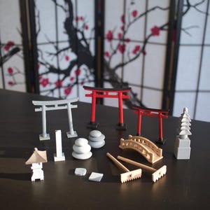 May include: A set of miniature Japanese garden elements, including two red torii gates, two gray torii gates, a gray pagoda, a gray stone lantern, a wooden bridge, a rake, and three stacks of gray stones.