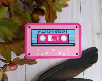 May include: A pink cassette tape sticker with the text "MIXED EMOTIONS" in black lettering. The cassette tape has a blue and black design.
