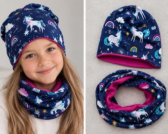 May include: A navy blue beanie and matching infinity scarf set featuring a repeating pattern of white unicorns, colorful rainbows, pink clouds, and yellow stars. Both items are lined with a solid bright pink fabric on the interior.